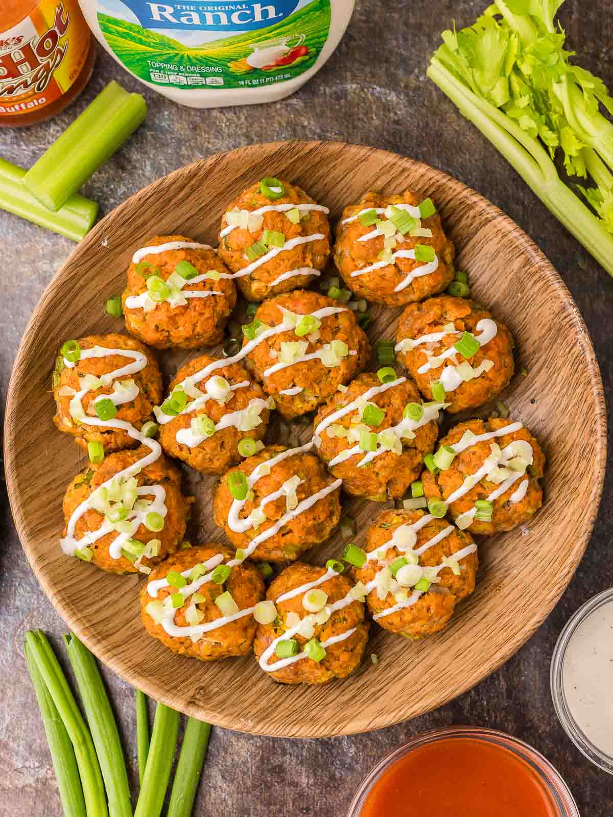 Buffalo Chicken Meatballs in a wooden bowl with ranch sauce drizzled on top.