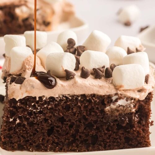 A sliced of Hot Chocolate Poke Cake with some chocolate sauce being poured on top.