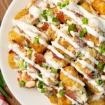 Up close of Loaded Tater Tots on a white plate with queso, bacon and Green onions.