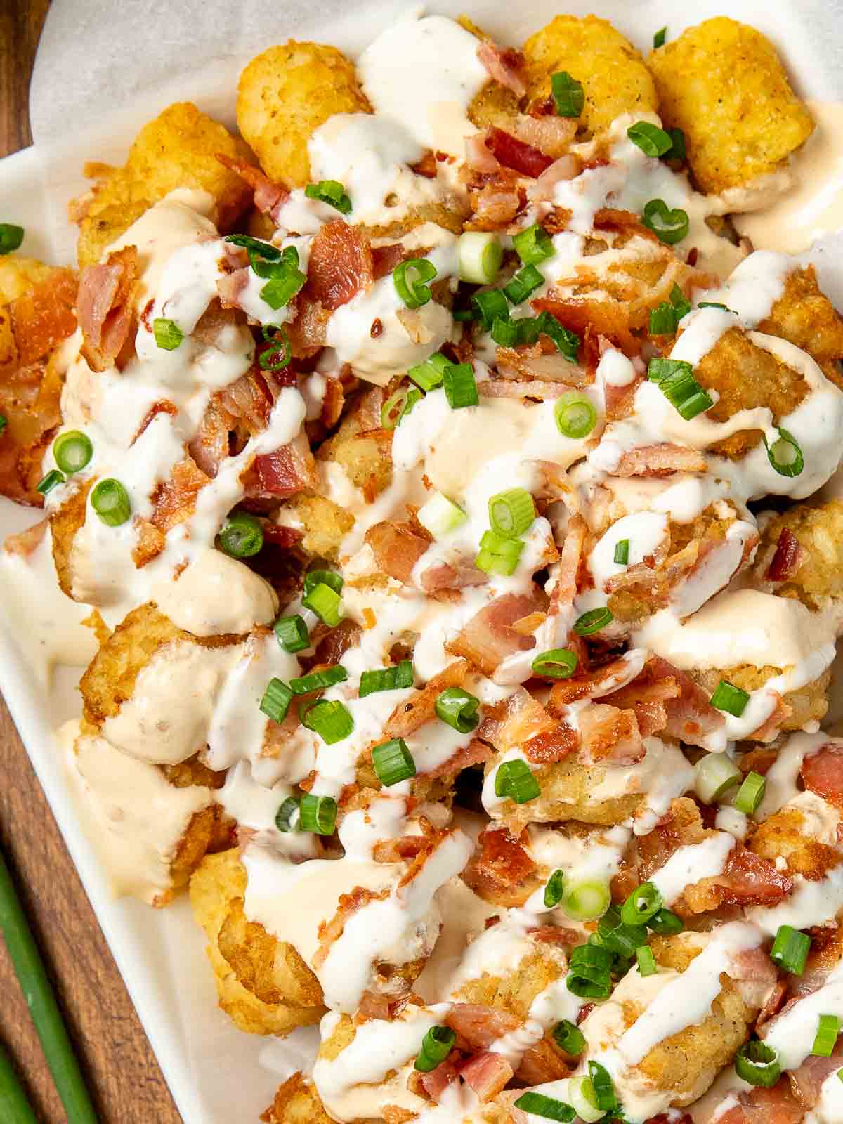 Up close of Loaded Tater Tots on a white plate with queso, bacon and Green onions.