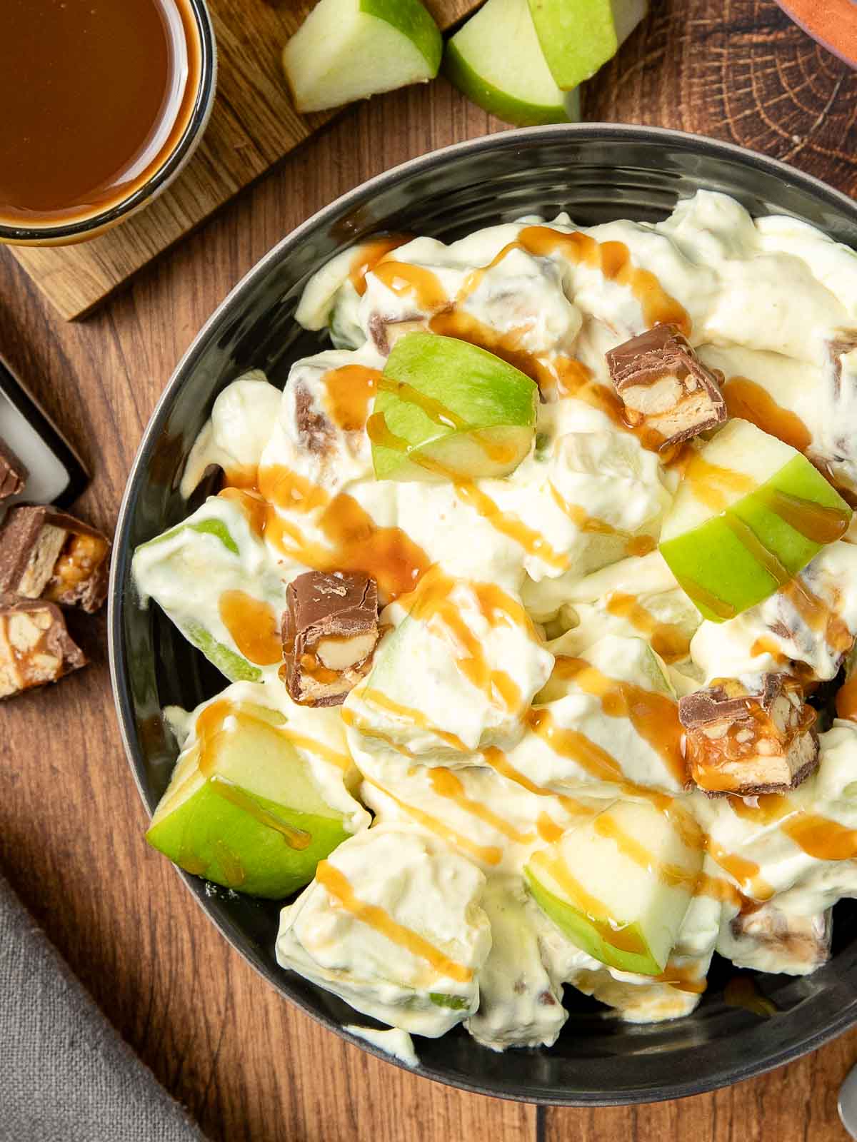 Up close of Snickers Salad in a black bowl on a wooden table.