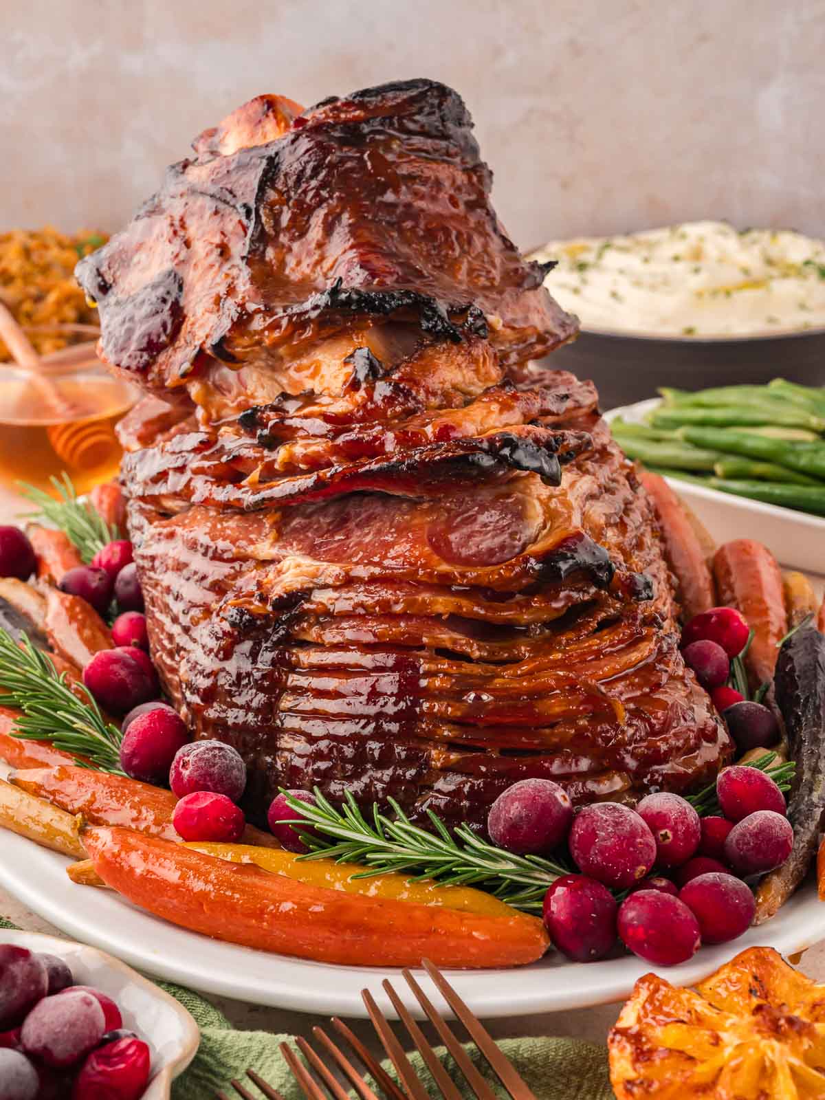 Glazed Ham on a serving dish with roasted carrots and herbs.