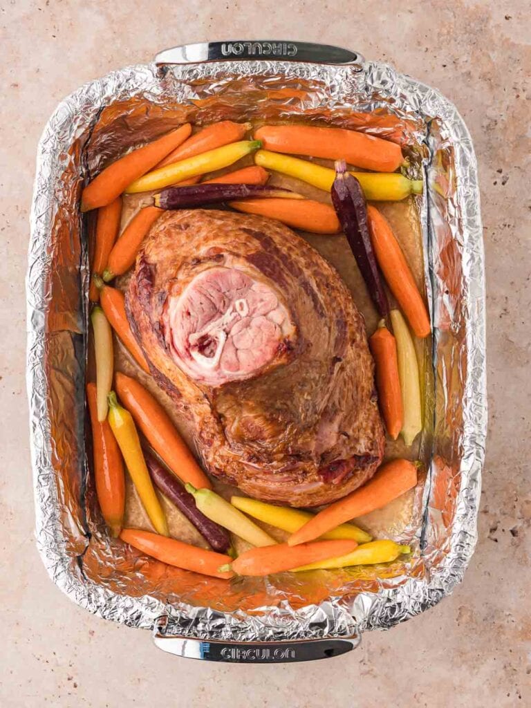 A ham and Carrots in a roasting tray with foil in the bottom.