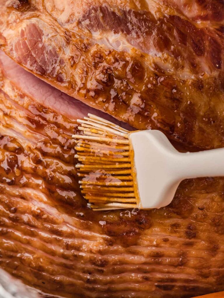 A white brush brushing glaze onto the ham.