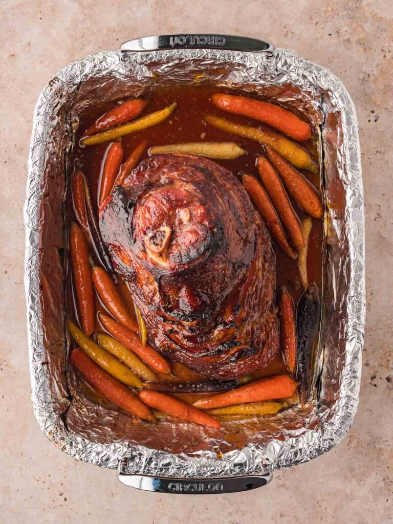 The fully cooked Glazed Ham with roasted Carrots ann around the bottom of the tray.