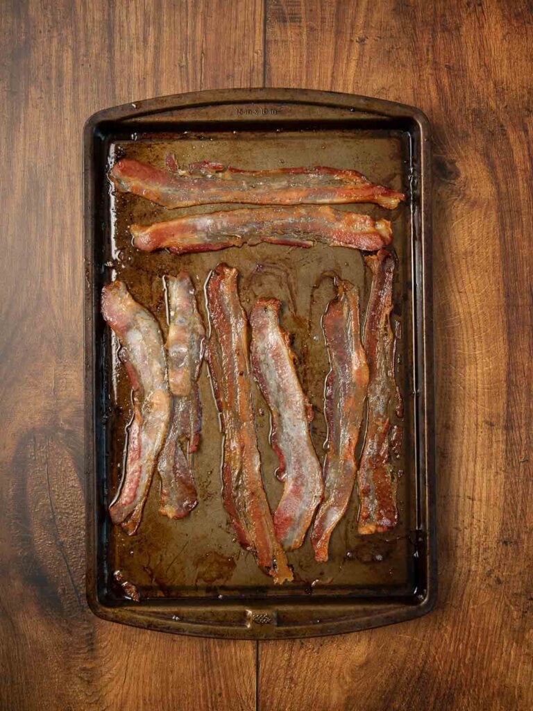 Cooked bacon on a baking tray on a wooden table.