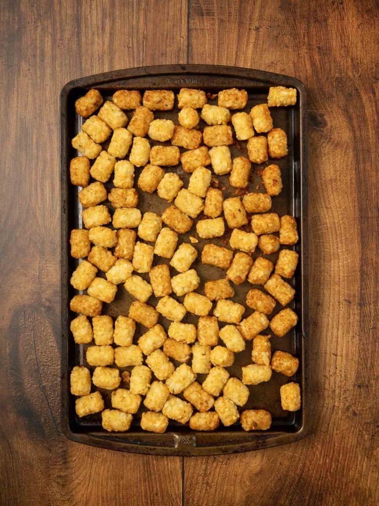 Cooked tater tots on a baking tray on a wooden table.