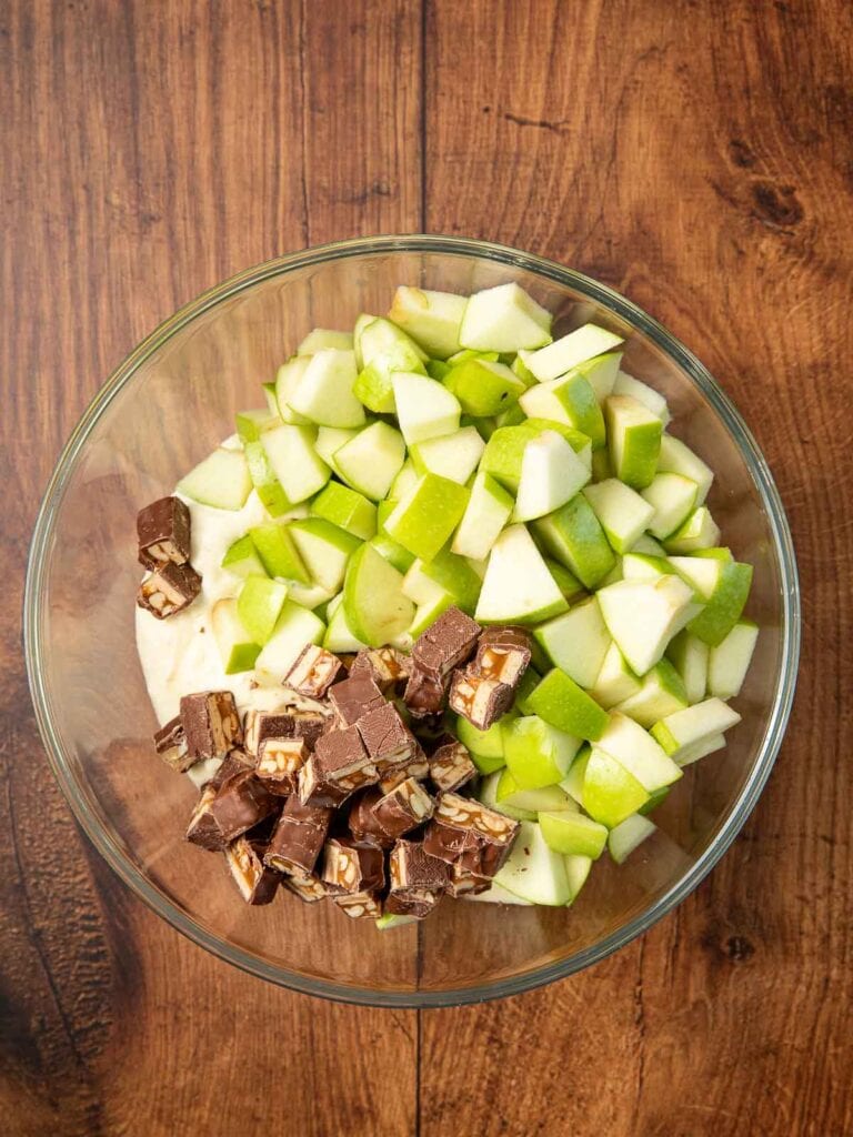 Chopped apple and snickers on top of the cool whip and pudding mixture in a bowl.