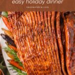 Close-up of glossy spiral-cut glazed ham slices with roasted carrots and rosemary by Tessie's Table.