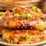 A plate full of honey garlic chicken wings with green onions on top.