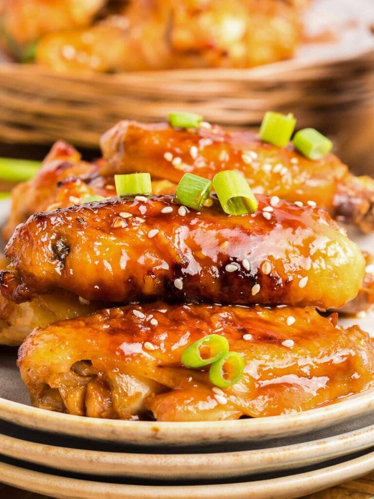 A plate full of honey garlic chicken wings with green onions on top.