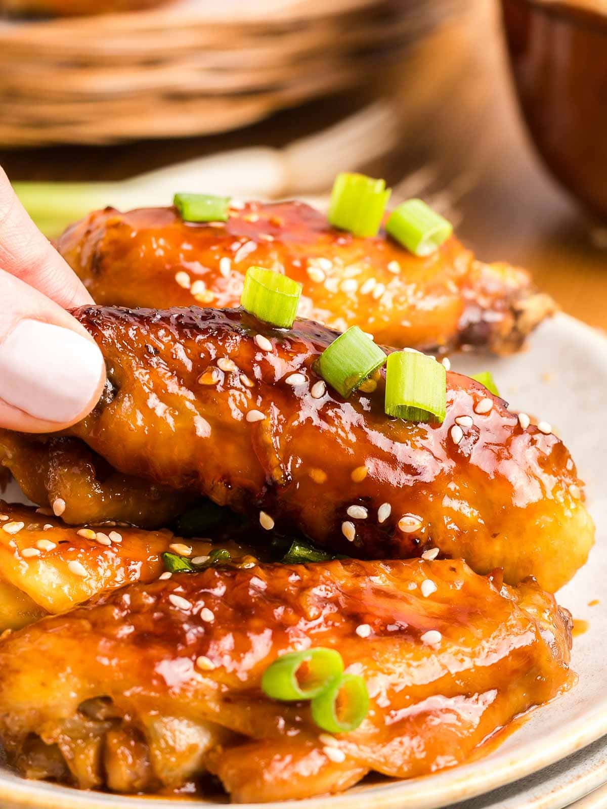 A honey garlic chicken wing being picked up by a hand with pale pink nail varnish.