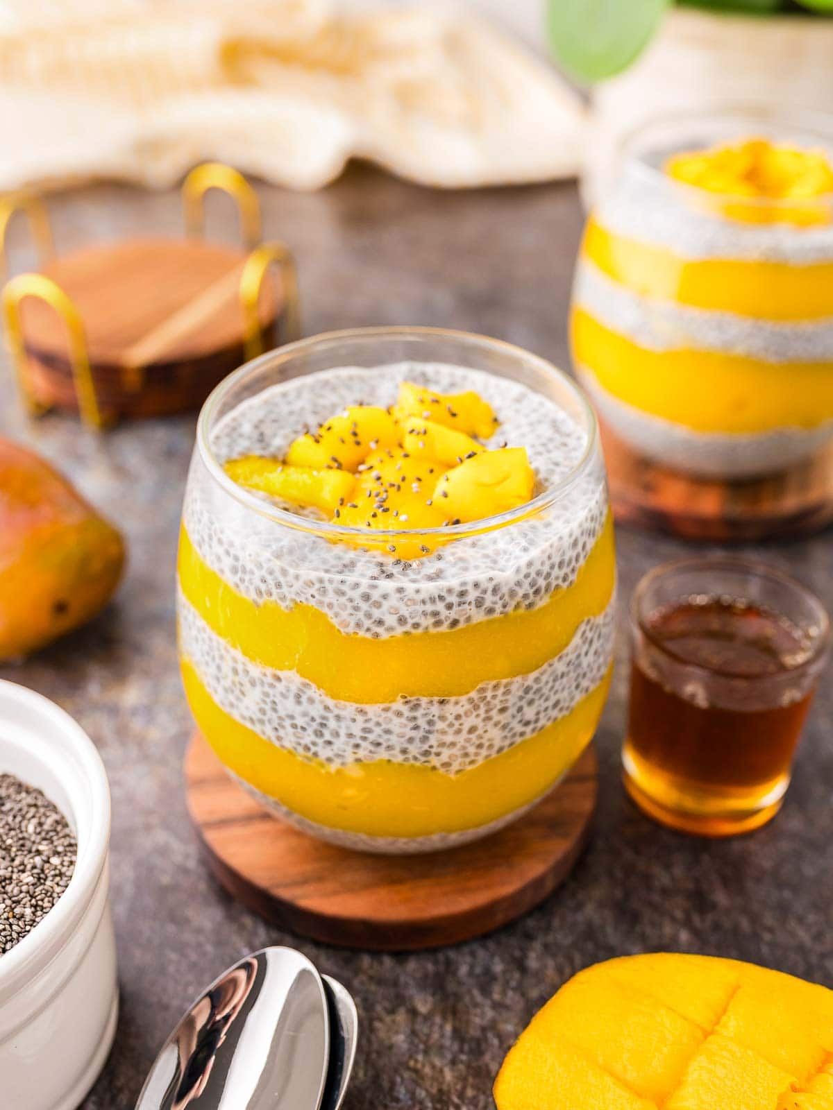 Two glasses with mango Chia Pudding layered up on a dark table.