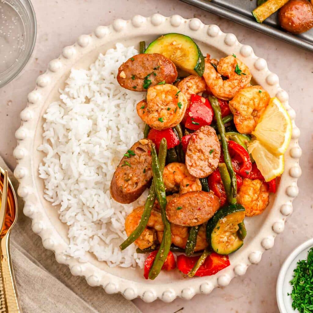 A white plate with shrimp and sausage with veggies served over rice.