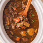 Over head shot of a ladle in a slow cooker with beef stew and fresh parsley.