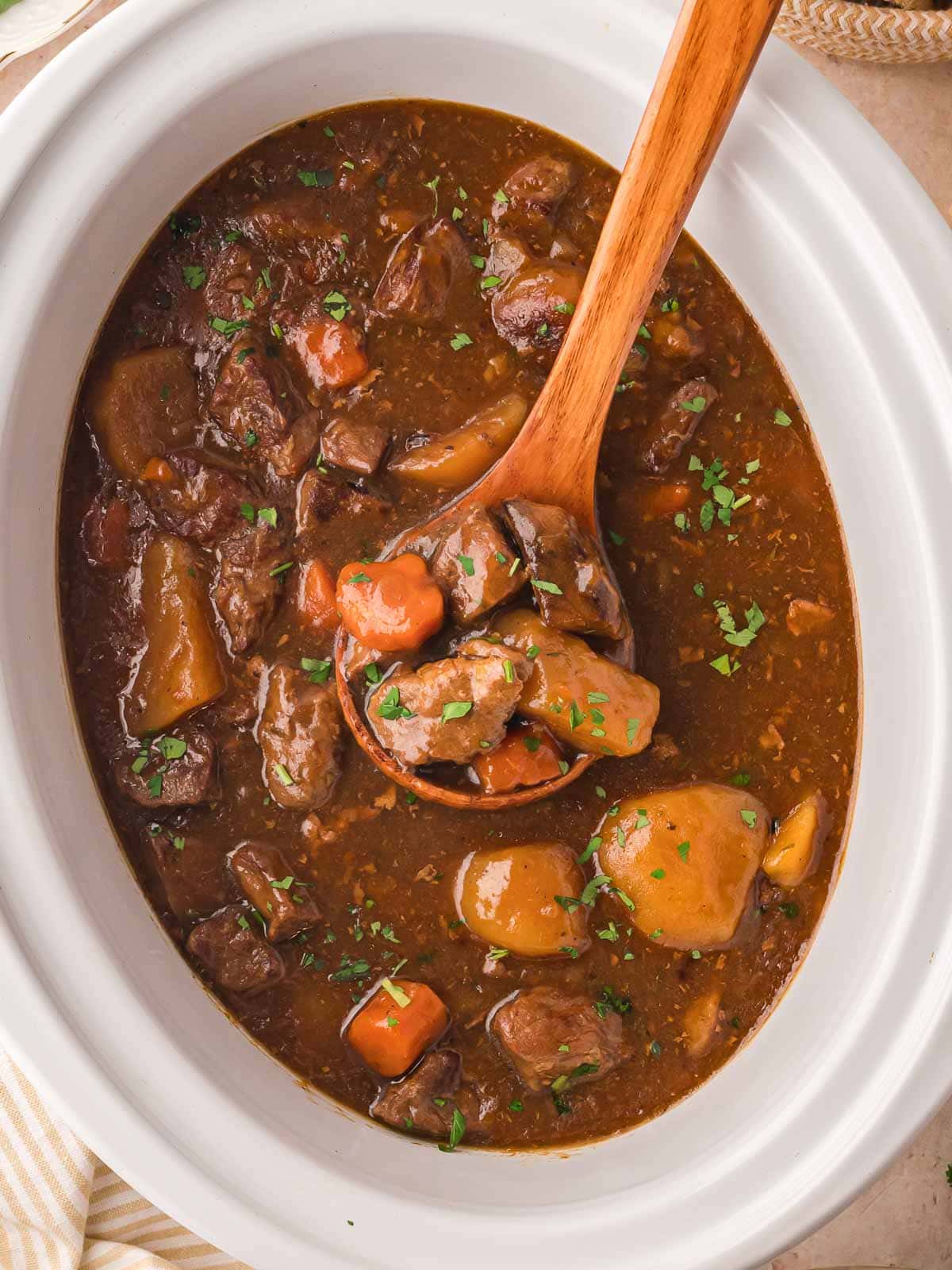 Over head shot of a ladle in a slow cooker with beef stew and fresh parsley.