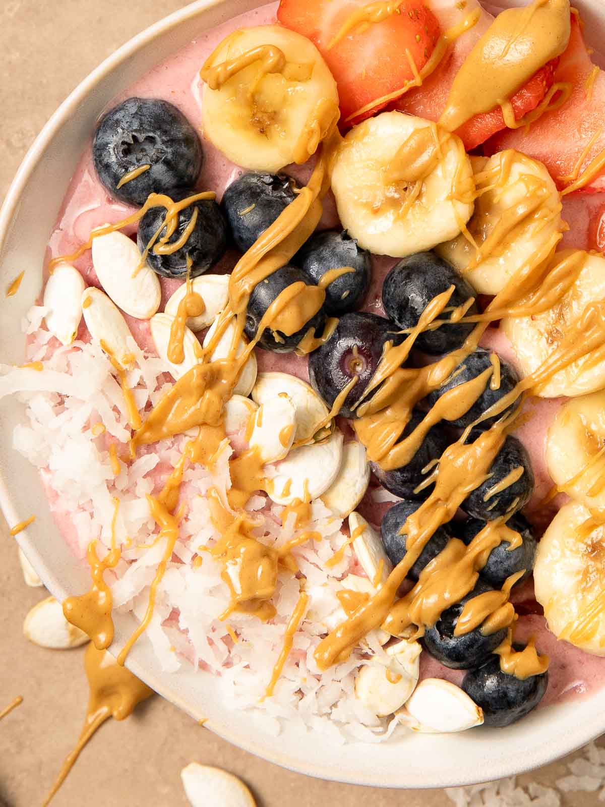 Up close of a smoothie Bowl with blueberries, coconut, banana, Strawberries and peanut butter on top.