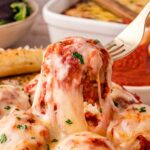 A fork lifting a a cheesy turkey meatball up from a plate of turkey meatball casserole.