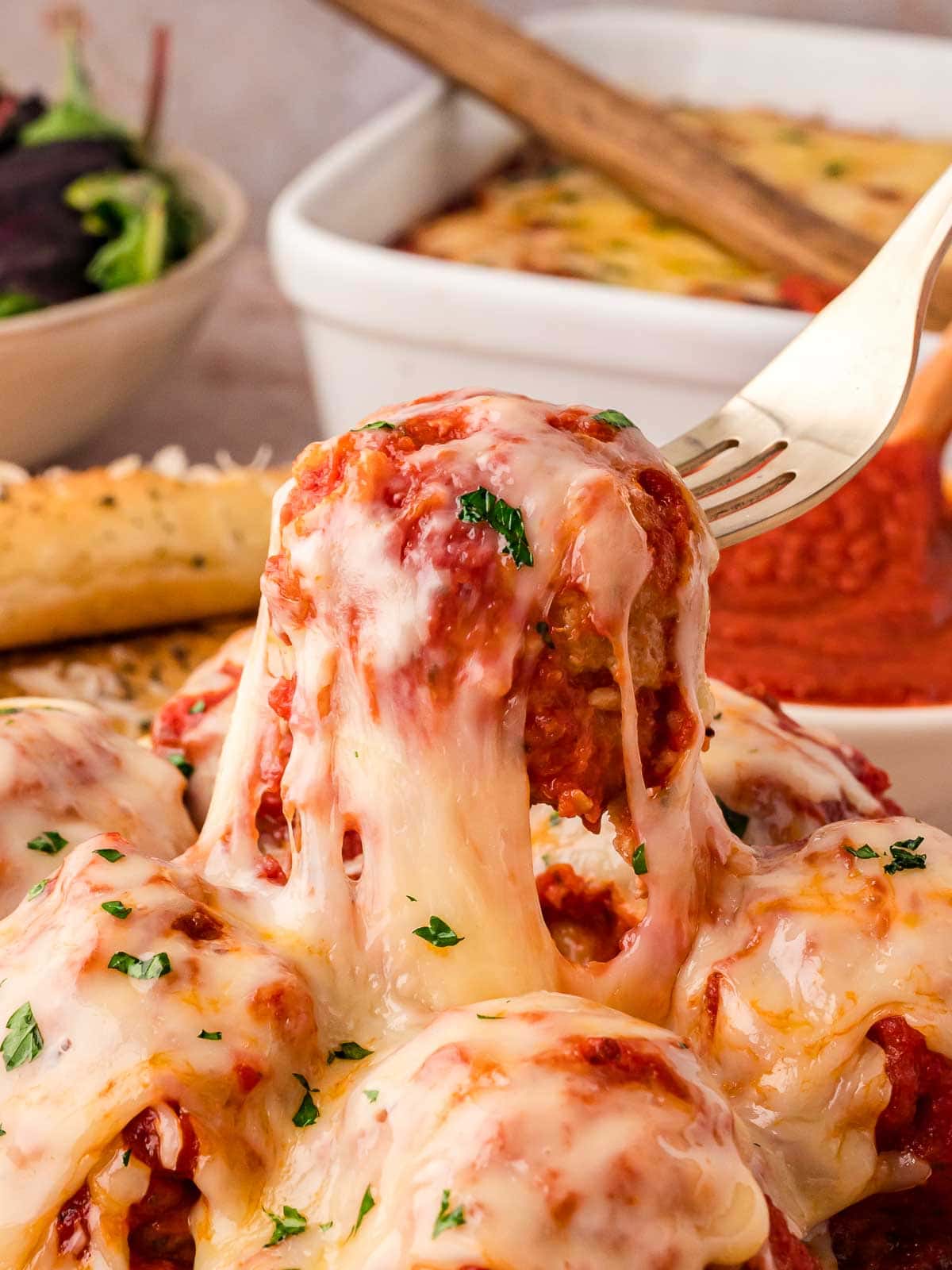 A fork lifting a a cheesy turkey meatball up from a plate of turkey meatball casserole.