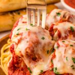 A fork placed in a turkey meatball with melted cheese and parsley on top.