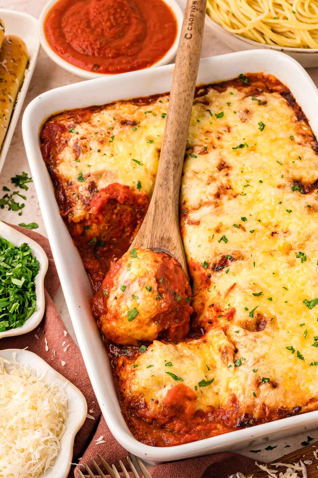 Large casserole dish with a wooden spoon taking a meatball out of the turkey meatball casserole.