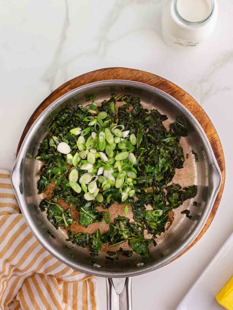 Wilted kale in a pot with green onions.