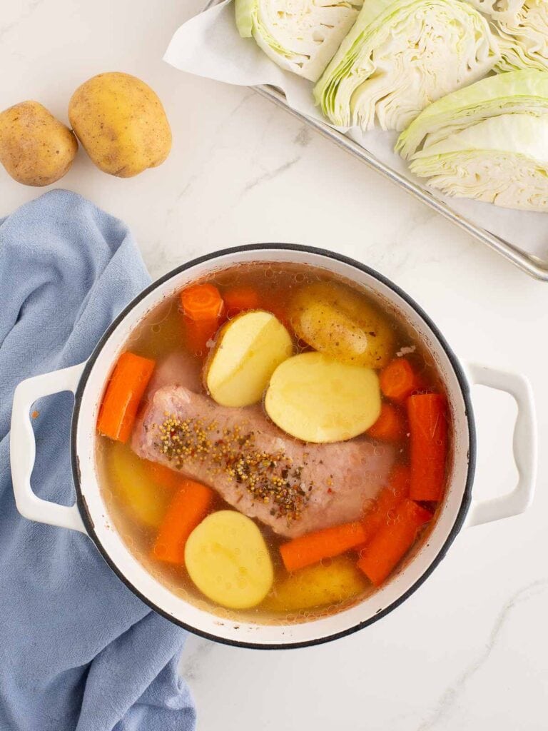 Potatoes and carrots in the pot with the corned beef and water.