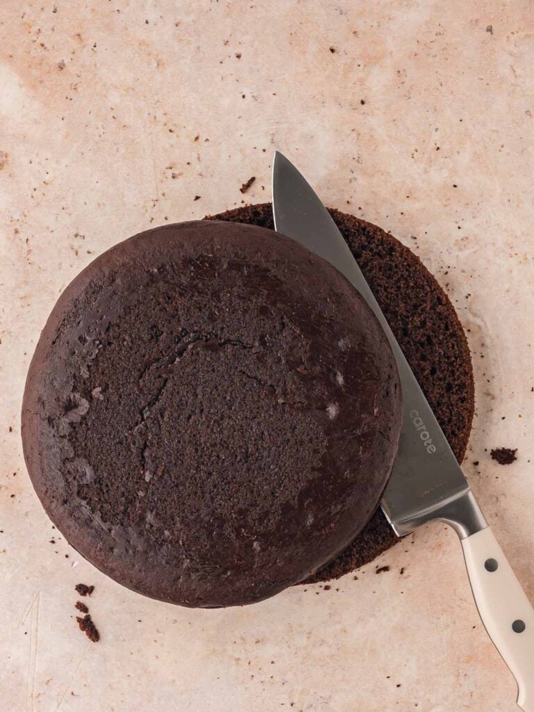 The dome shape being cut off the top of a double chocolate cake.