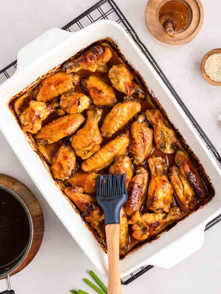 Cooked chicken wings in a casserole with the honey garlic sauce seing brushed on.