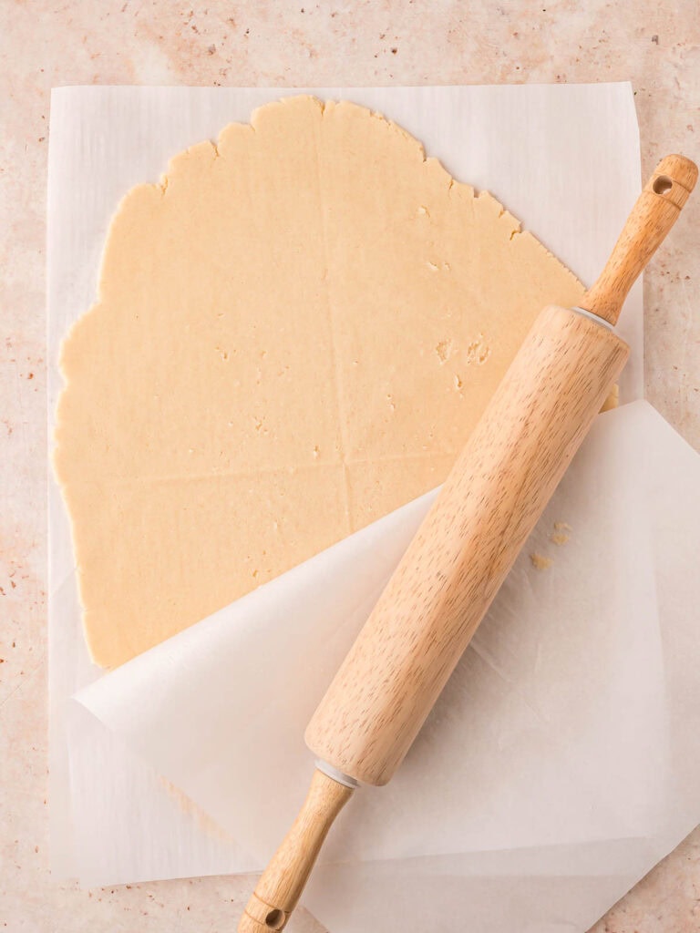 Shortbread cookie dough rolled out between two sheets of parchment paper.