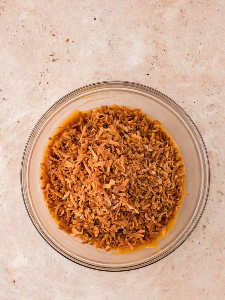 Toasted coconut being mixed in the bowl with the melted caramel.