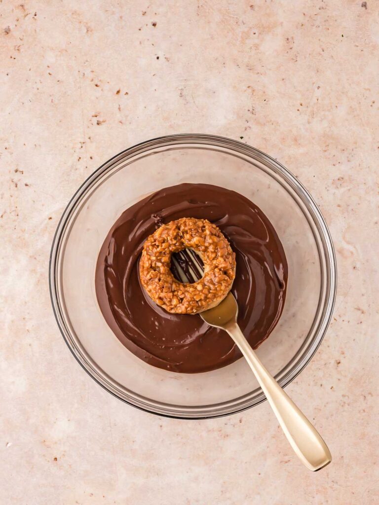 Samoas cookies being dipped into the melted chocolate.