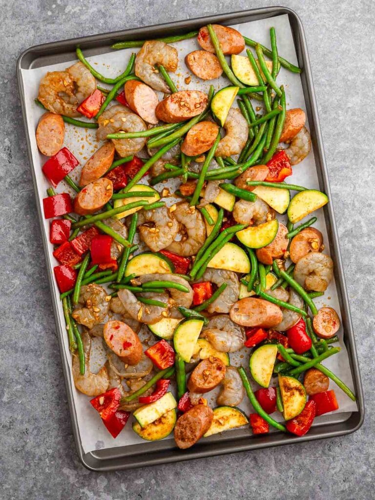 All the raw shrimp and veggies with the sauce on a sheet pan.