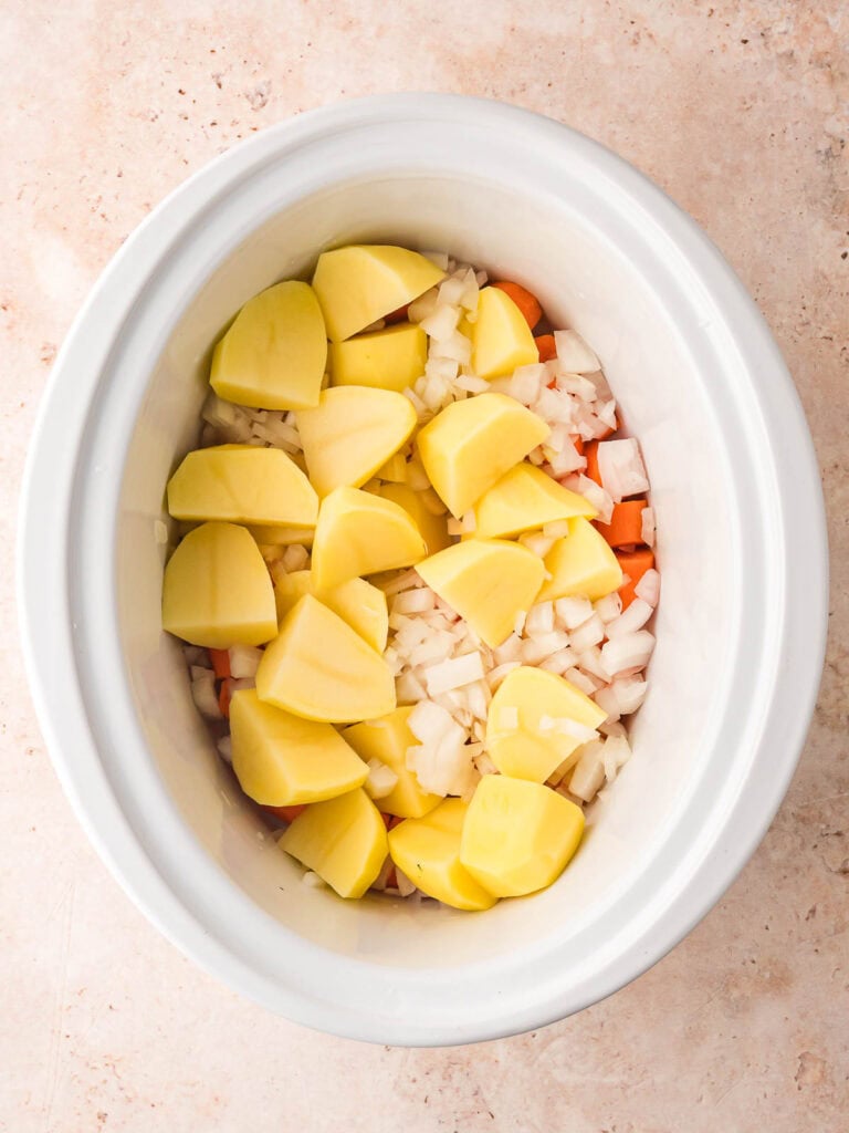 Vegetables and potatoes in a white slow cooker.