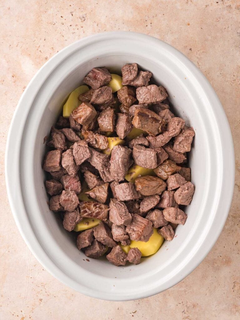 Vegetable, potaatoes and browned beef in a white slow cooker.