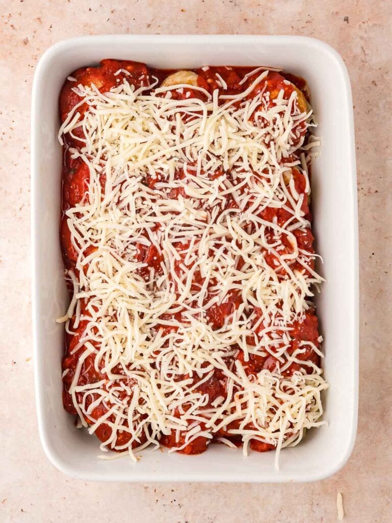 Grated cheese on top of the marinara sauce with the turkey meatballs in a casserole dish.