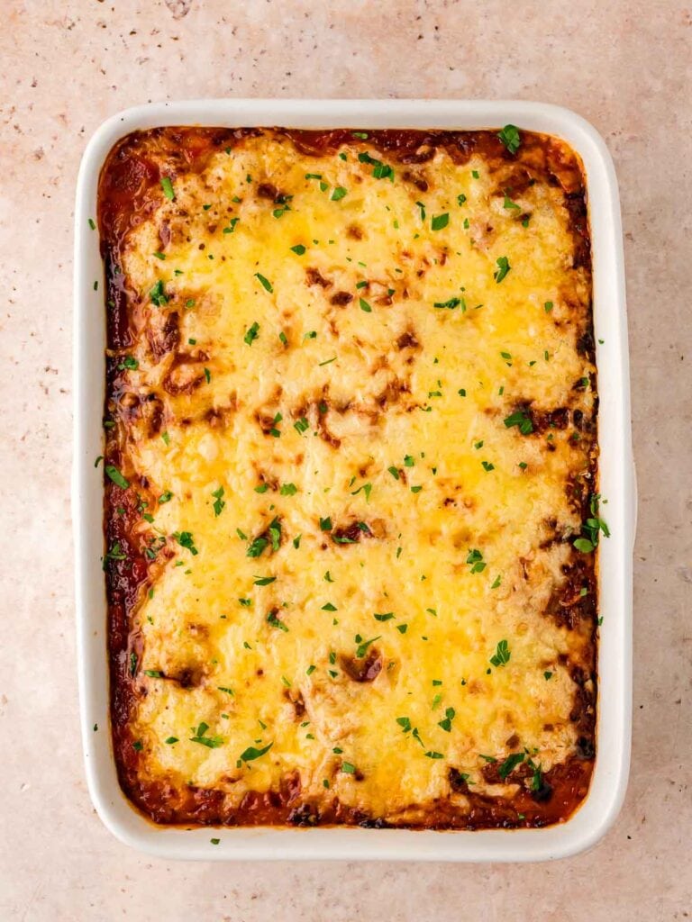 Full cooked turkey meatball casserole with melted cheese and chopped parsley on top.