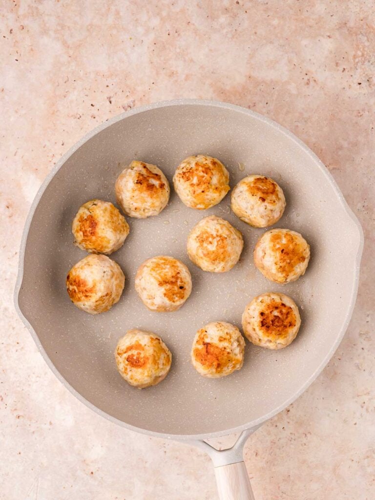 Meatballs being browned in a pan.