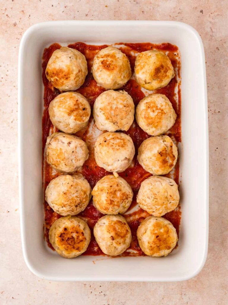 Marinara sauce and turkey meatballs layered in a casserole dish.