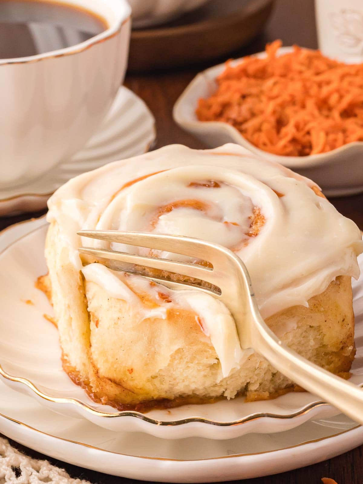 A fork slicing into a carrot cake cinnamon roll.