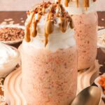 Two mason jars filled with carrot cake overnight oats with greek yogurt on top and peanut butter dripping down the side of the glass.