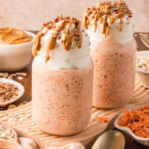 Two mason jars filled with carrot cake overnight oats with greek yogurt on top and peanut butter dripping down the side of the glass.