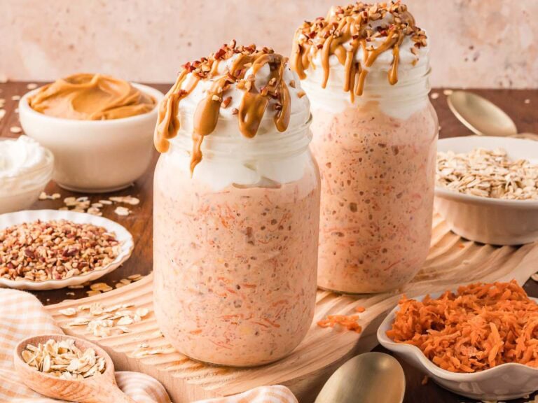 Two mason jars filled with carrot cake overnight oats with greek yogurt on top and peanut butter dripping down the side of the glass.