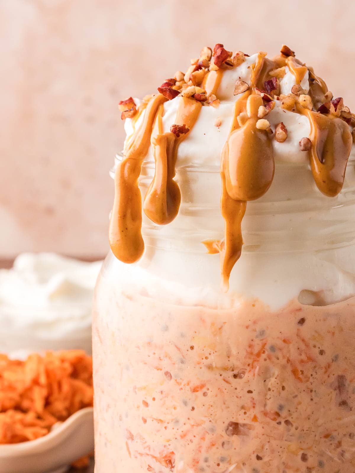 Up close of carrot cake overnight oats with greek yogurt on top and peanut butter dripping down the side of the glass.