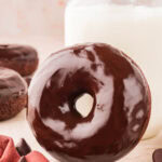 A chocolate glazed donut leaning up against a glass of milk.