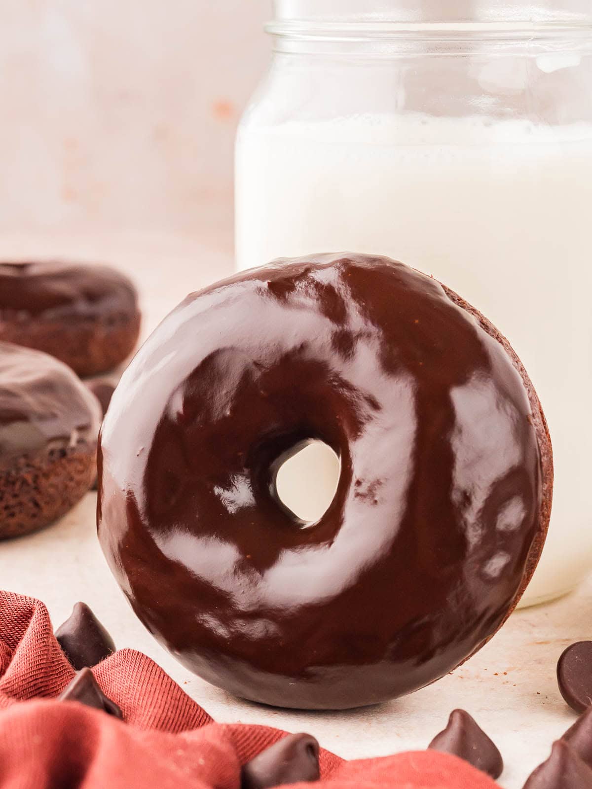 A chocolate glazed donut leaning up against a glass of milk.