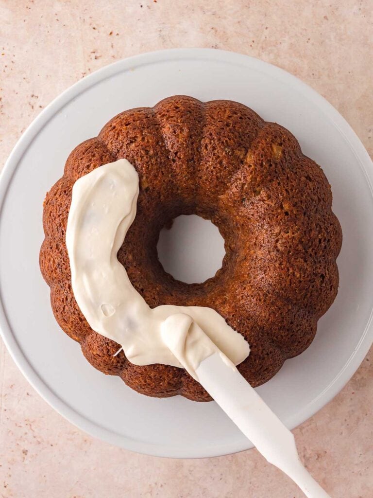 Cream cheese glaze being spread onto the carrot bundt cake.