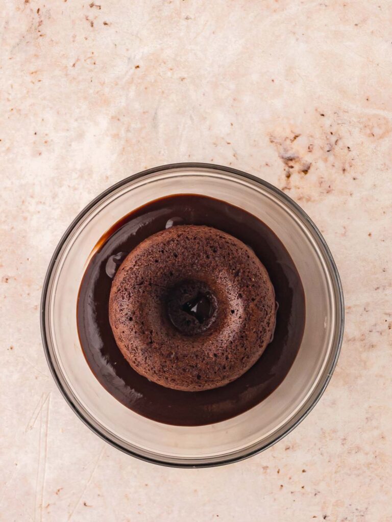 Double chocolate donut being dipped in a bowl of ganache.