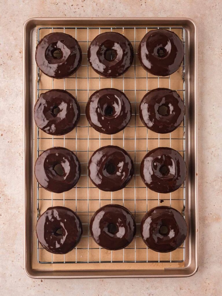 Double Chocolate donuts glazed with ganache on a wire rack.