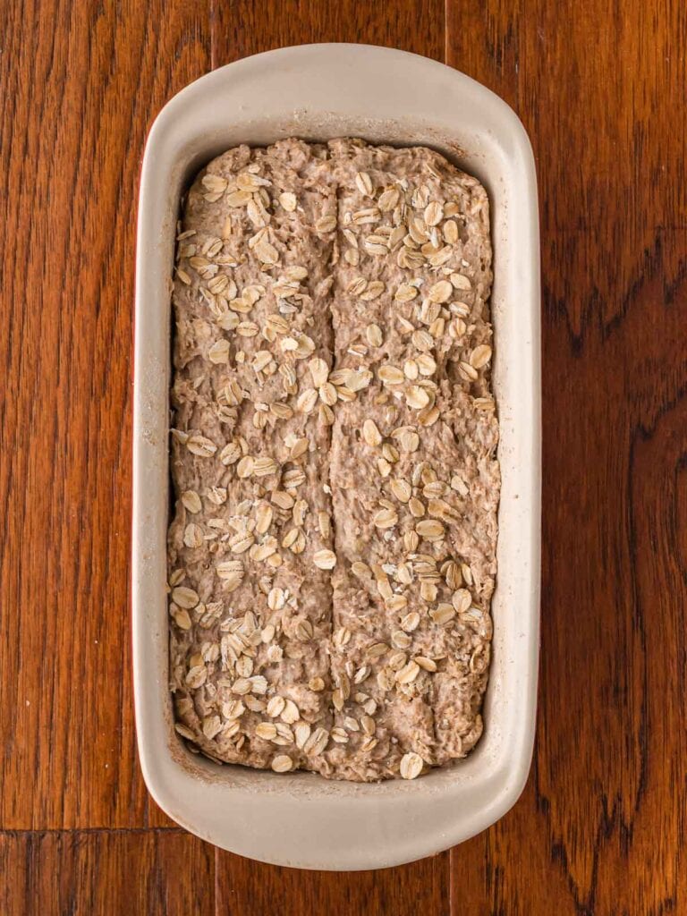 Raw brown bread on in a bread pan on a wooden table.